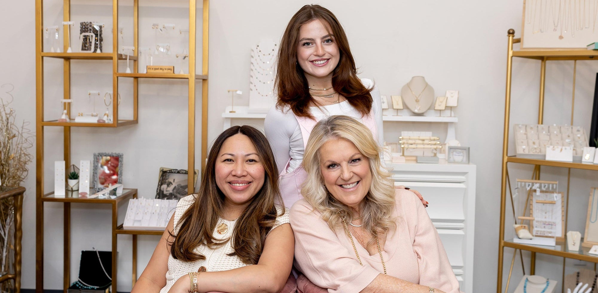 Three women sitting together in a stylish interior setting with shelves and decor.